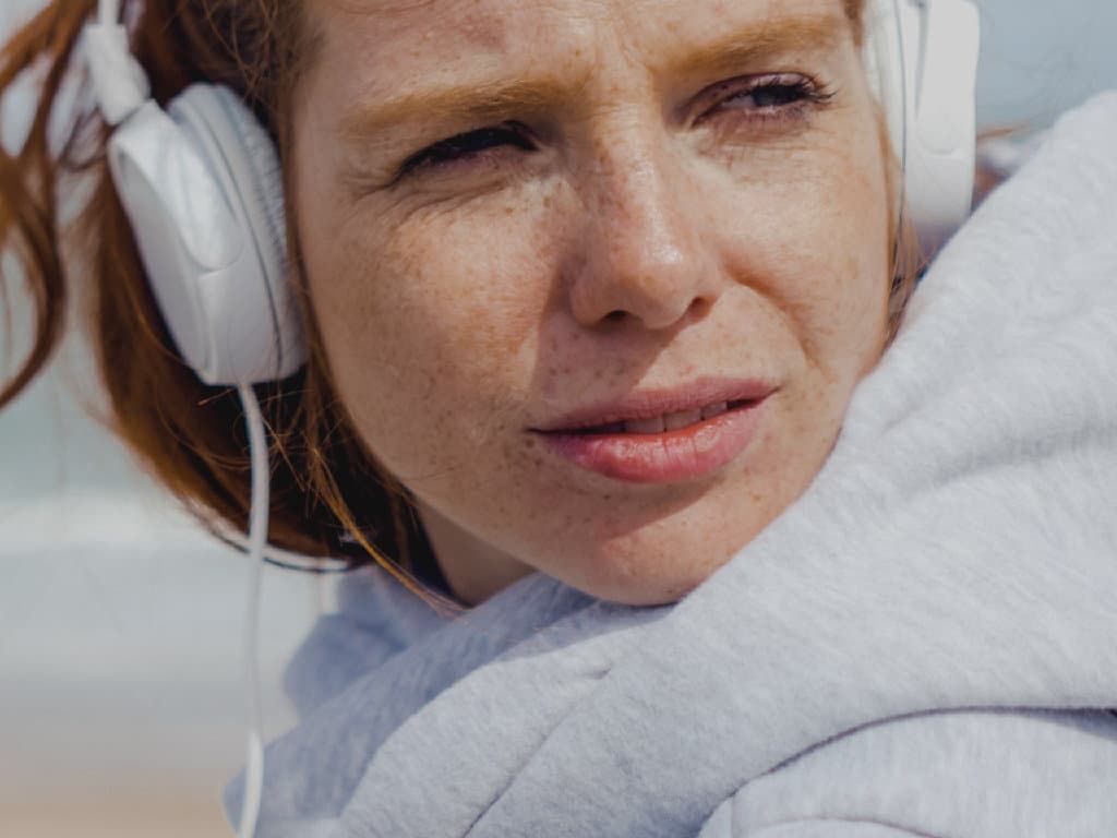 Sieviete ar austiņām atpūšas pludmalē, baudot sauli un viļņu skaņas