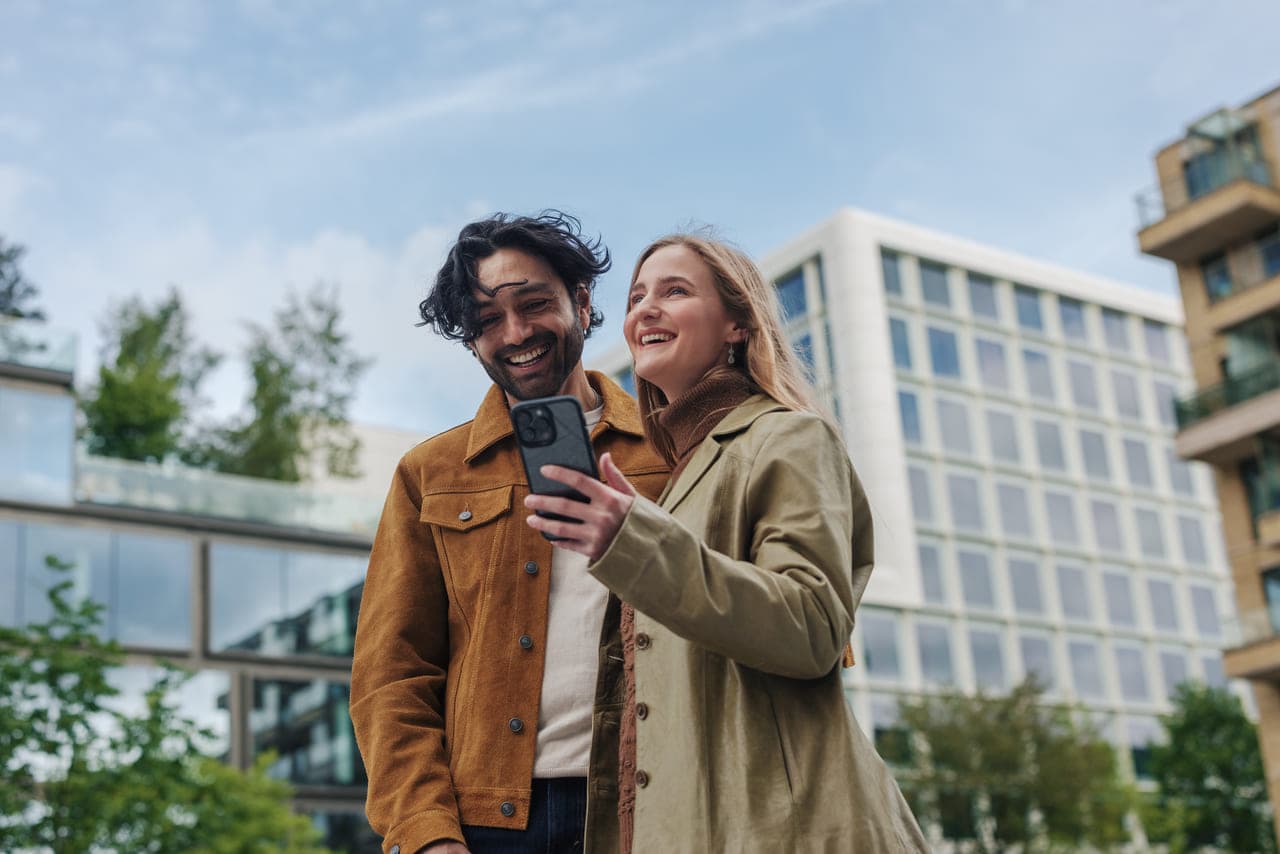 Vīrietis un sieviete smaidoši uzņem pašbildi modernas ēkas priekšā